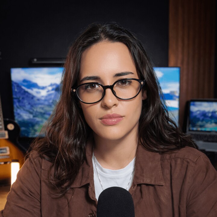 Sophia Scatola, mentora do Máquina de MRR, de óculos, sentada na bancada de trabalho com um microfone à frente.